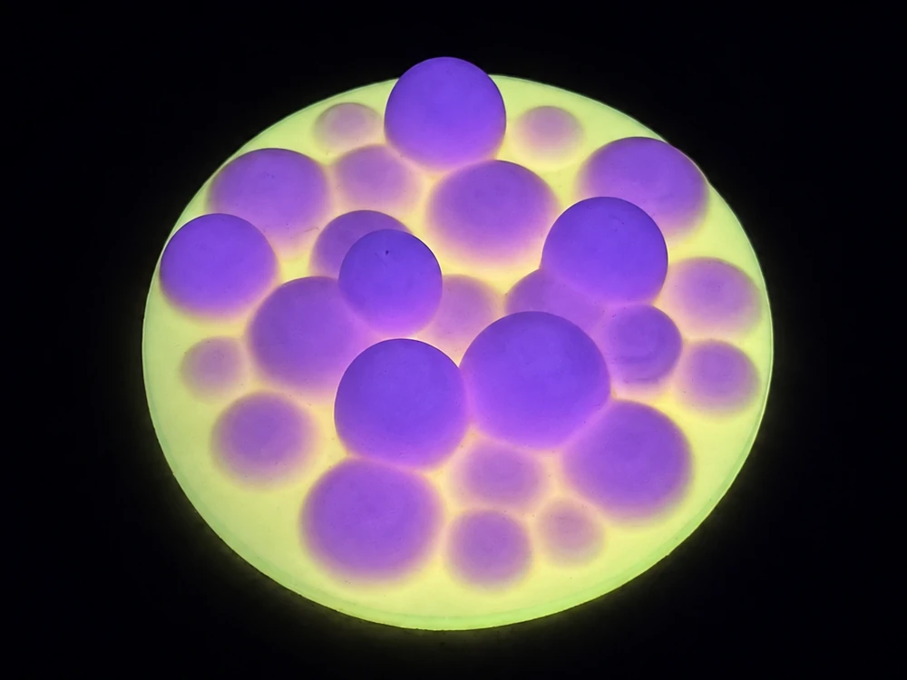 Rainbow bubble lid photographed in the dark, with purple bubbles against a glowing yellow-green base.