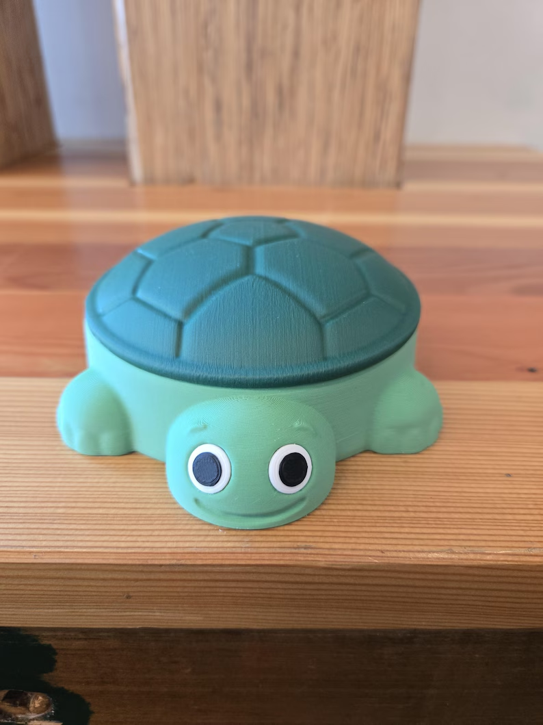 A green turtle sandbox with its teal shell lid closed.